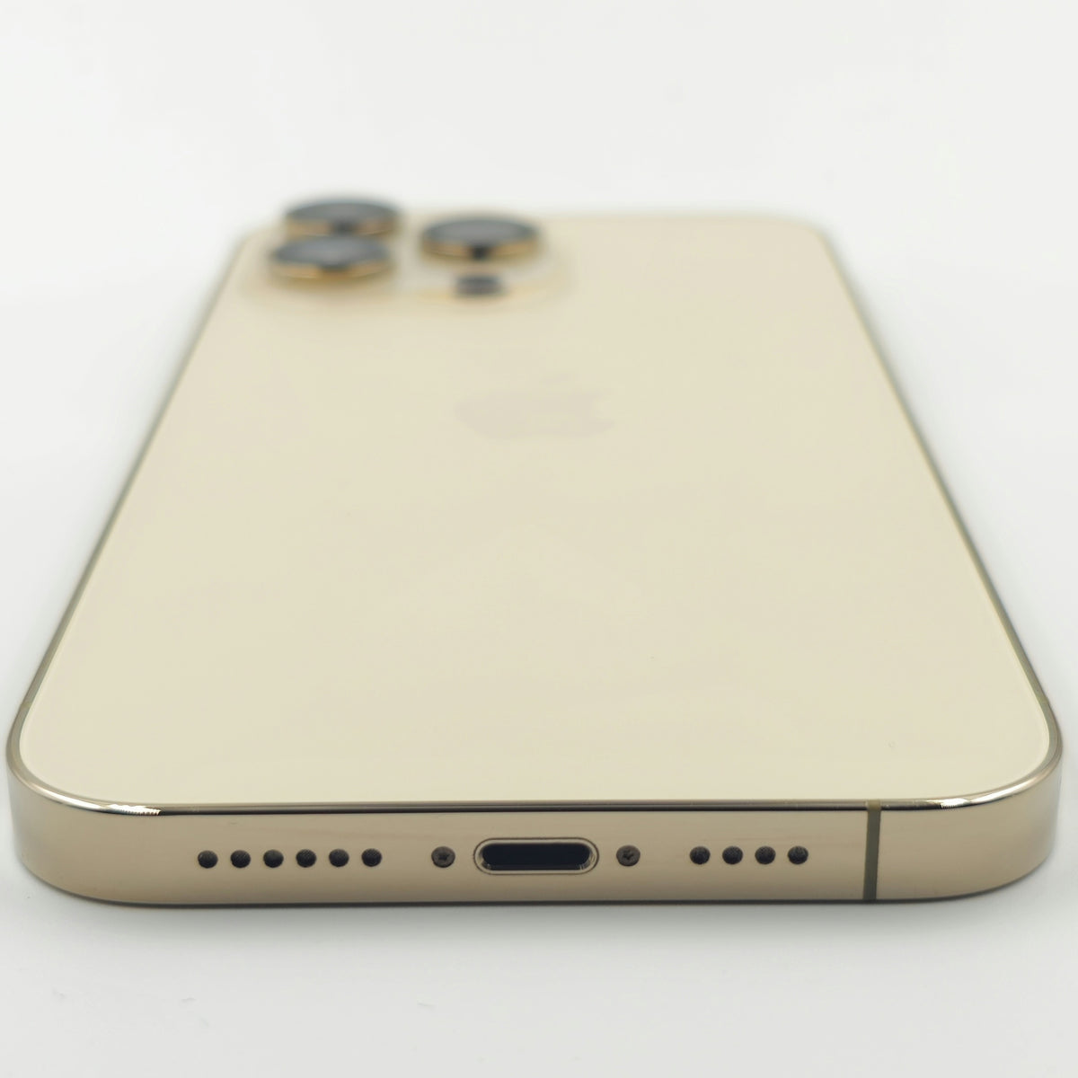 A close-up shot of the back of a gold-colored Apple iPhone 14 Pro Max, showing the camera lenses, speaker grille, charging port and bottom edge on a white background.