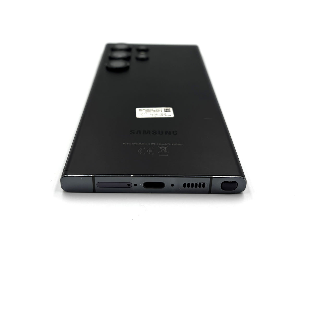 The back of a black Samsung S23 Ultra smartphone, showing the rear camera array, a small sticker, and the SAMSUNG logo, photographed on a clean white background.
