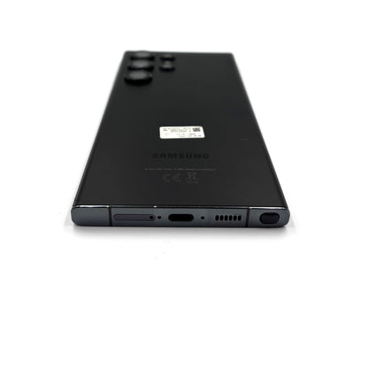 The back of a black Samsung S23 Ultra smartphone, showing the rear camera array, a small sticker, and the SAMSUNG logo, photographed on a clean white background.