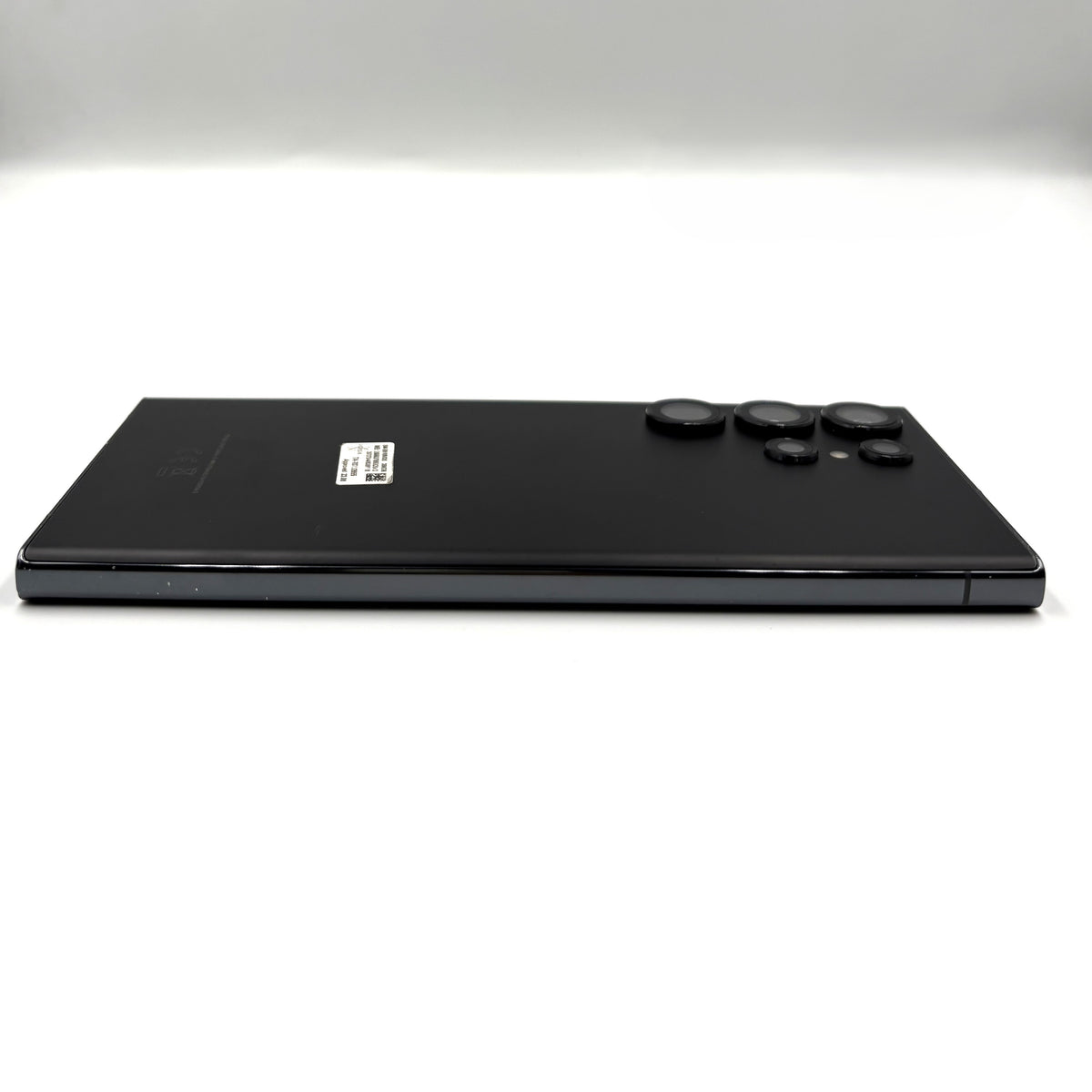 A black Samsung Galaxy S23 Ultra device shown from the back, positioned horizontally against a clean white studio background.