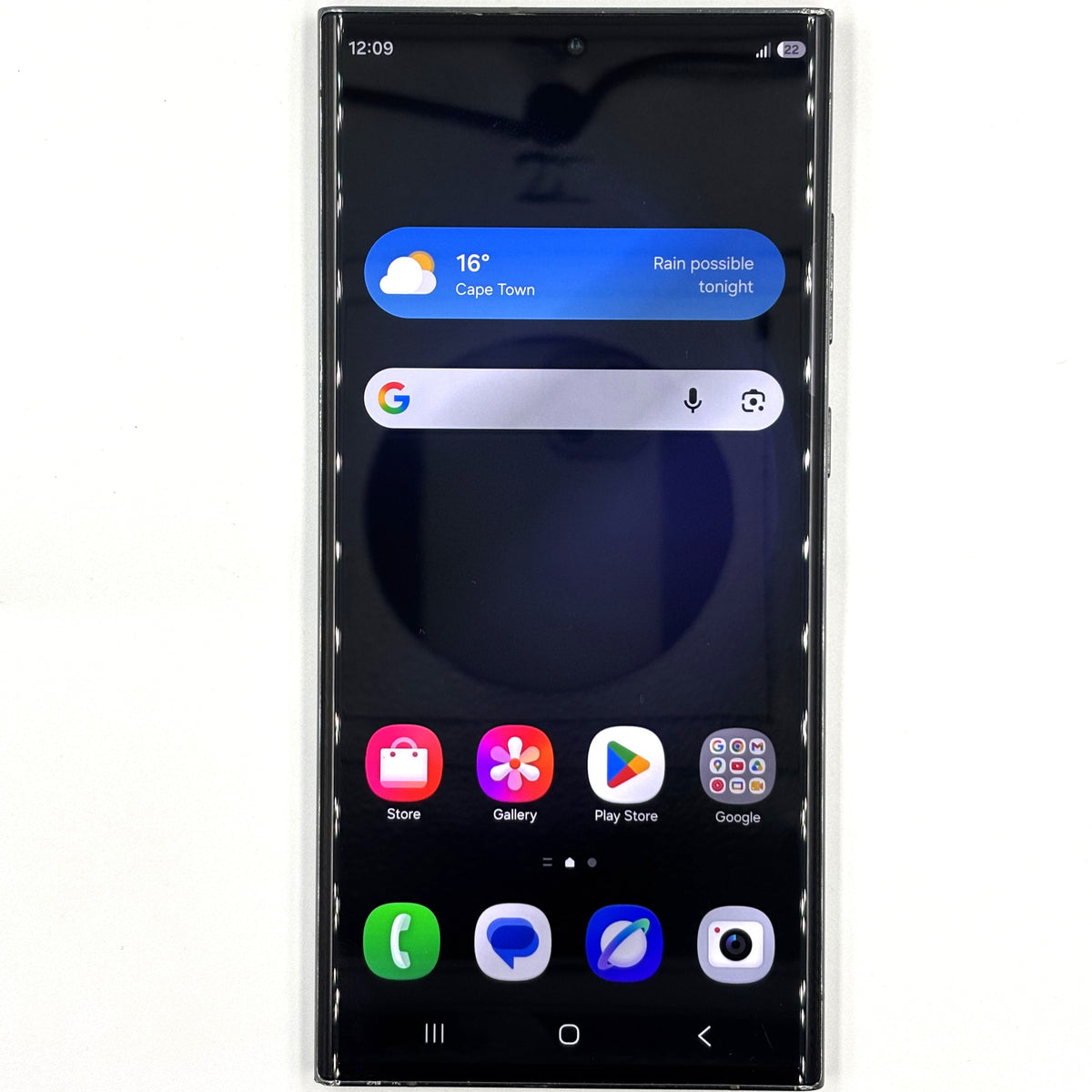 A black Samsung Galaxy S23 Ultra smartphone shown from the front on a plain white background, with the home screen active and displaying weather, search bar, app icons, and status bar details.
