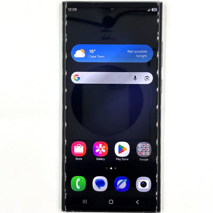 A black Samsung Galaxy S23 Ultra smartphone shown from the front on a plain white background, with the home screen active and displaying weather, search bar, app icons, and status bar details.