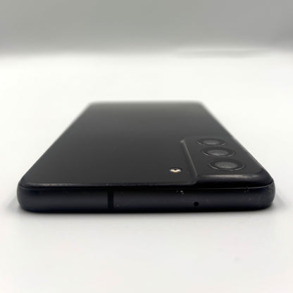 A black smartphone shown from the back, photographed on a plain light gray to white studio background. The back panel is matte black with a raised camera module containing three circular lenses and a small gold accent near the top.