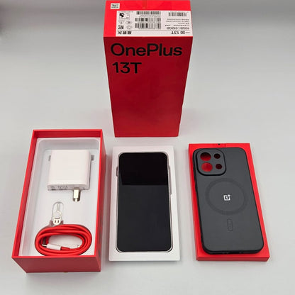 OnePlus 13T smartphone shown with its red retail box, white charging adapter, red cable, and a black MagSafe case on a light gray surface.