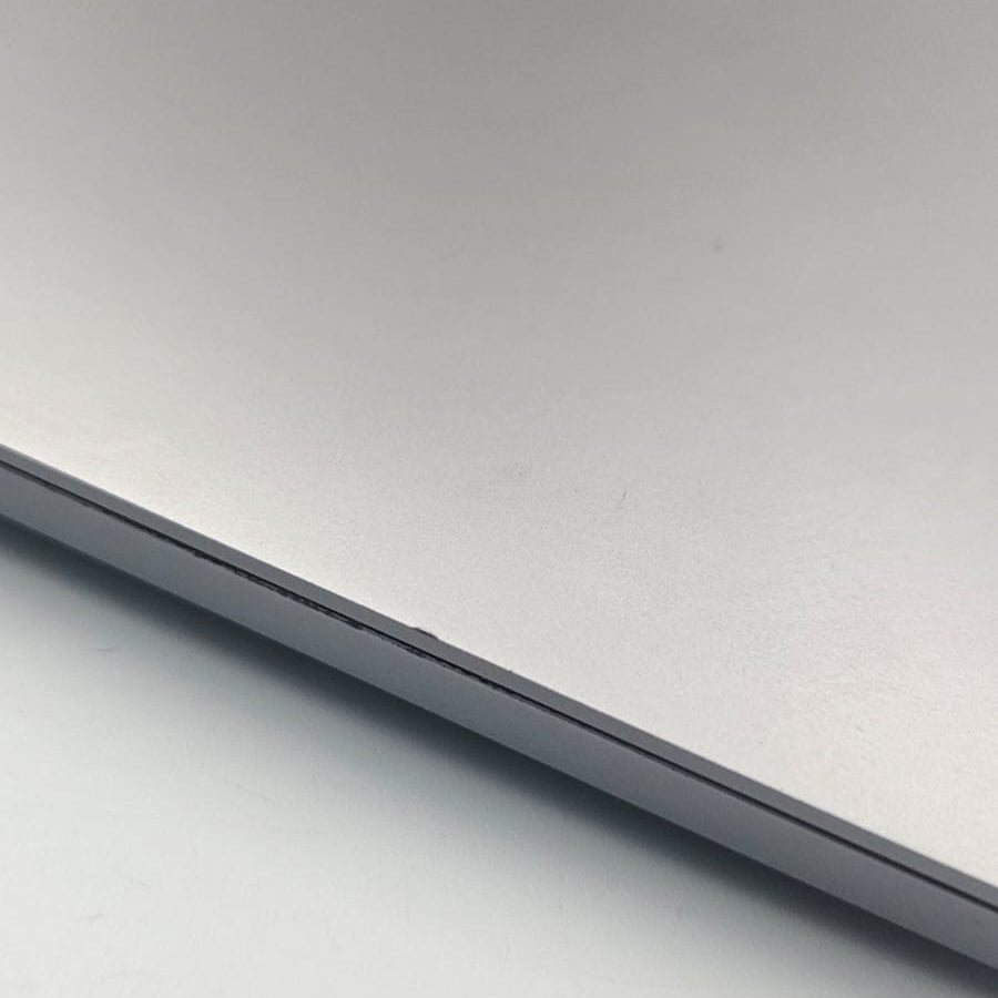 Close-up of a silver aluminum MacBook Pro lid with the Apple logo visible in the upper left corner, resting on a light gray surface.