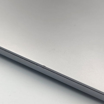 Close-up of a silver aluminum MacBook Pro lid with the Apple logo visible in the upper left corner, resting on a light gray surface.