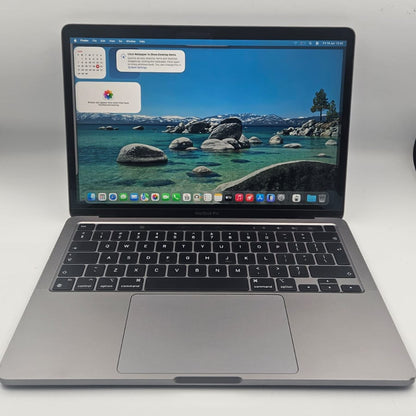 A silver Apple MacBook laptop with an open screen displaying a scenic lake wallpaper, set against a plain light gray background.